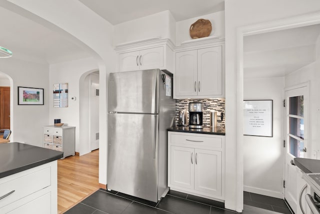 kitchen with dark tile patterned flooring, white cabinets, tasteful backsplash, and stainless steel refrigerator