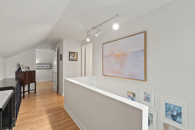 hallway featuring vaulted ceiling, rail lighting, and light hardwood / wood-style flooring