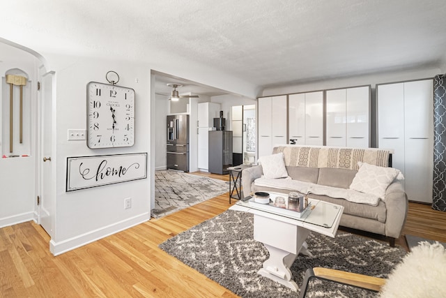 living room with ceiling fan, a textured ceiling, and light hardwood / wood-style flooring