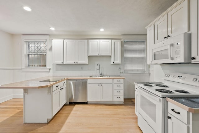 kitchen featuring light wood-style flooring, a peninsula, a sink, and white appliances