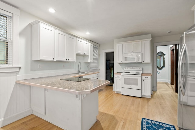 kitchen featuring white appliances, a peninsula, white cabinetry, a sink, and light wood finished floors