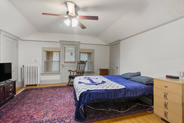 bedroom featuring a ceiling fan, radiator, light wood-style floors, and lofted ceiling