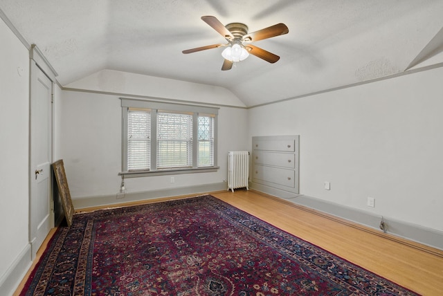 unfurnished bedroom featuring vaulted ceiling, a textured ceiling, radiator, ceiling fan, and wood finished floors