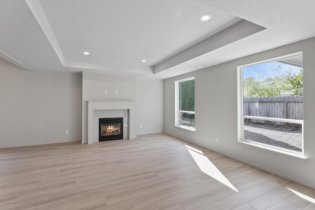 unfurnished living room with light hardwood / wood-style floors and a tray ceiling