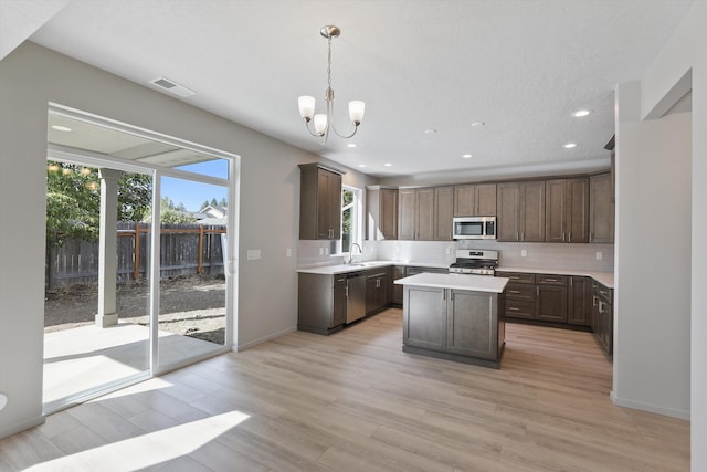 kitchen with pendant lighting, appliances with stainless steel finishes, a kitchen island, a notable chandelier, and light wood-type flooring