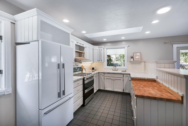 kitchen with white fridge, white cabinetry, a skylight, range with two ovens, and wood counters