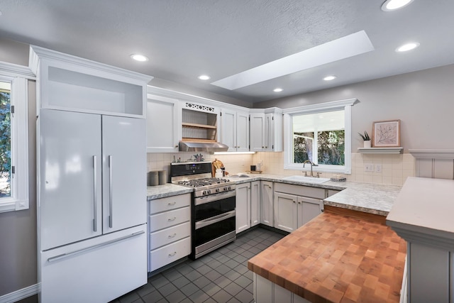 kitchen with white cabinets, wood counters, range with two ovens, paneled built in refrigerator, and sink