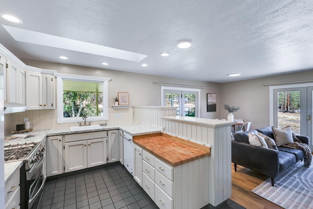 kitchen with a skylight, kitchen peninsula, stainless steel appliances, white cabinets, and sink