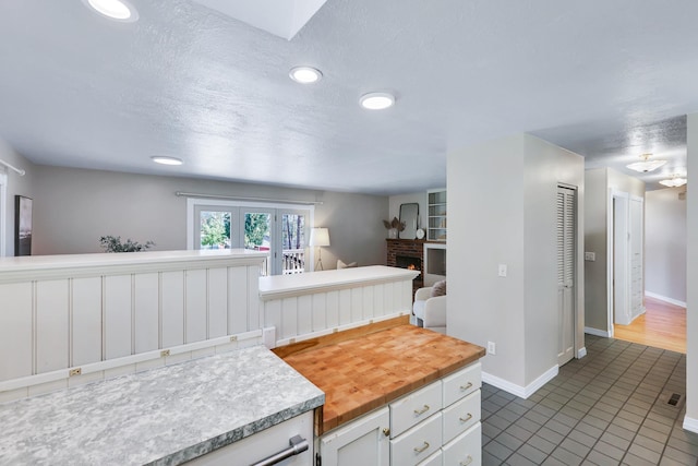 kitchen with dark tile patterned flooring, a textured ceiling, wooden counters, white cabinetry, and a fireplace