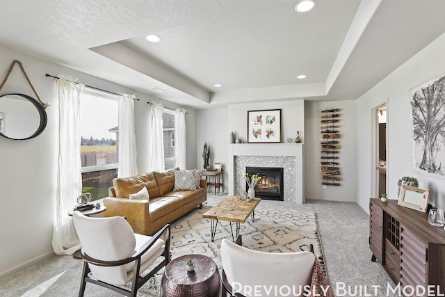 living room featuring light colored carpet, a tile fireplace, a tray ceiling, and a textured ceiling