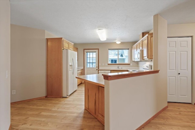 kitchen featuring a textured ceiling, white appliances, light brown cabinets, kitchen peninsula, and light wood-type flooring