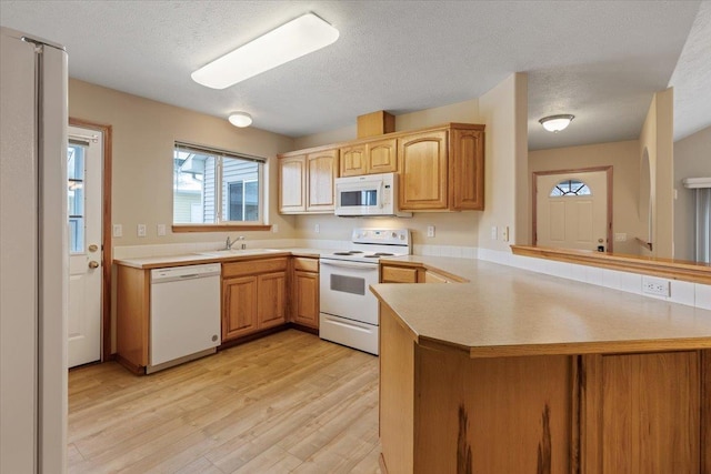 kitchen with white appliances, a textured ceiling, light hardwood / wood-style floors, sink, and kitchen peninsula