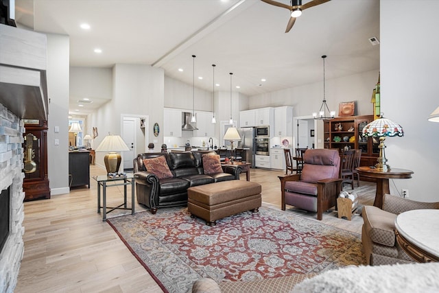 living room with ceiling fan with notable chandelier, light wood-type flooring, a fireplace, high vaulted ceiling, and beam ceiling