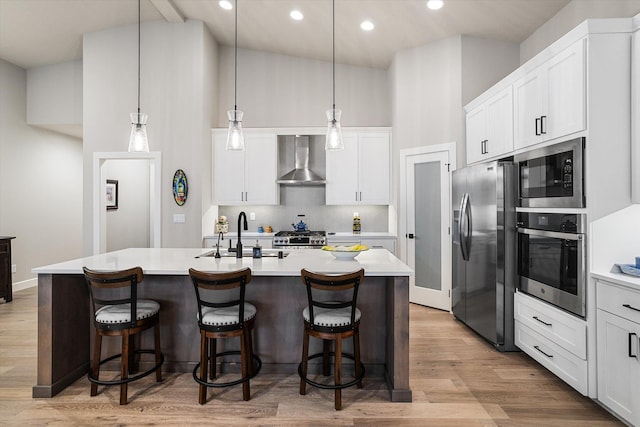 kitchen featuring sink, wall chimney range hood, appliances with stainless steel finishes, and an island with sink