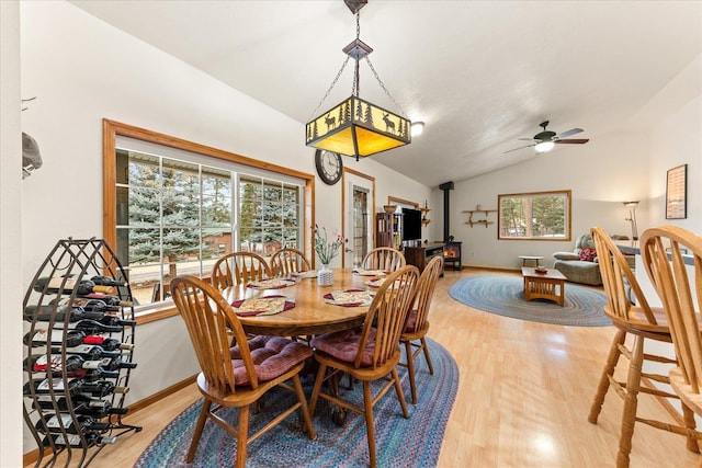 dining room with lofted ceiling, ceiling fan, plenty of natural light, and a wood stove