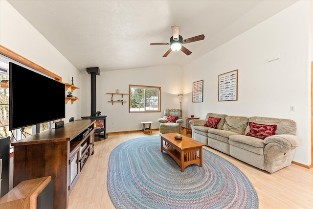 living room featuring ceiling fan, vaulted ceiling, a wood stove, and light hardwood / wood-style floors