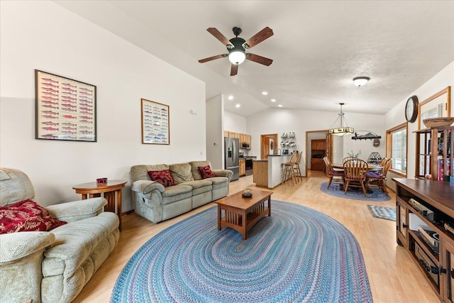 living room featuring lofted ceiling, light wood-type flooring, a textured ceiling, and ceiling fan