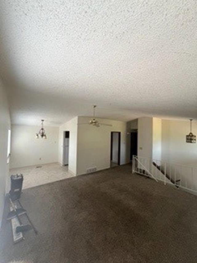 unfurnished living room with carpet, ceiling fan with notable chandelier, and a textured ceiling