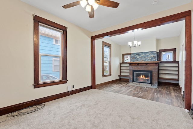 unfurnished living room featuring ceiling fan with notable chandelier and dark colored carpet