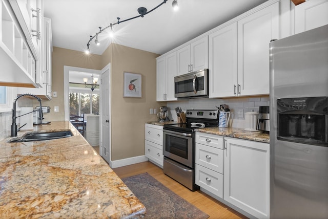 kitchen with white cabinetry, stainless steel appliances, light hardwood / wood-style flooring, light stone counters, and sink