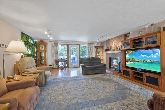 living room with a textured ceiling, a brick fireplace, track lighting, and hardwood / wood-style flooring