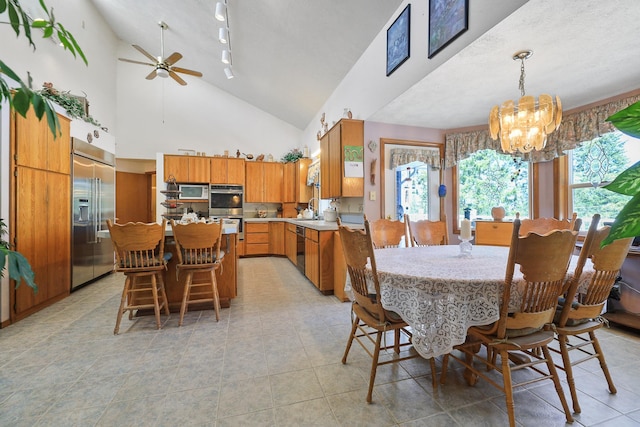 tiled dining space featuring sink, a textured ceiling, high vaulted ceiling, ceiling fan with notable chandelier, and rail lighting