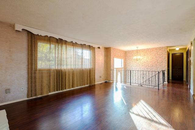 empty room with dark wood-type flooring and an inviting chandelier