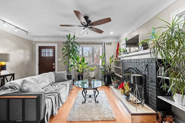 living room featuring ceiling fan, track lighting, hardwood / wood-style floors, and a brick fireplace