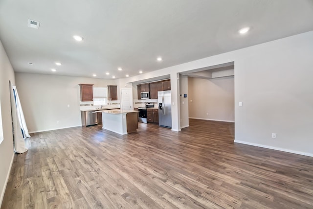 kitchen with dark hardwood / wood-style floors, decorative backsplash, sink, appliances with stainless steel finishes, and an island with sink