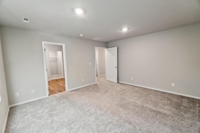 unfurnished bedroom with a closet, a walk in closet, and light colored carpet