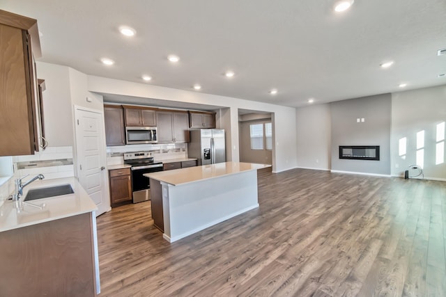 kitchen featuring appliances with stainless steel finishes, a kitchen island, tasteful backsplash, sink, and hardwood / wood-style flooring