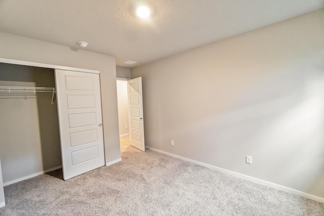 unfurnished bedroom featuring a textured ceiling, a closet, and light carpet