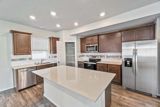 kitchen with dark hardwood / wood-style floors, a center island, decorative backsplash, sink, and appliances with stainless steel finishes