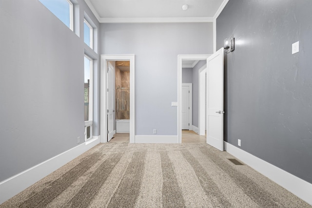 unfurnished bedroom with light colored carpet, multiple windows, crown molding, and a towering ceiling