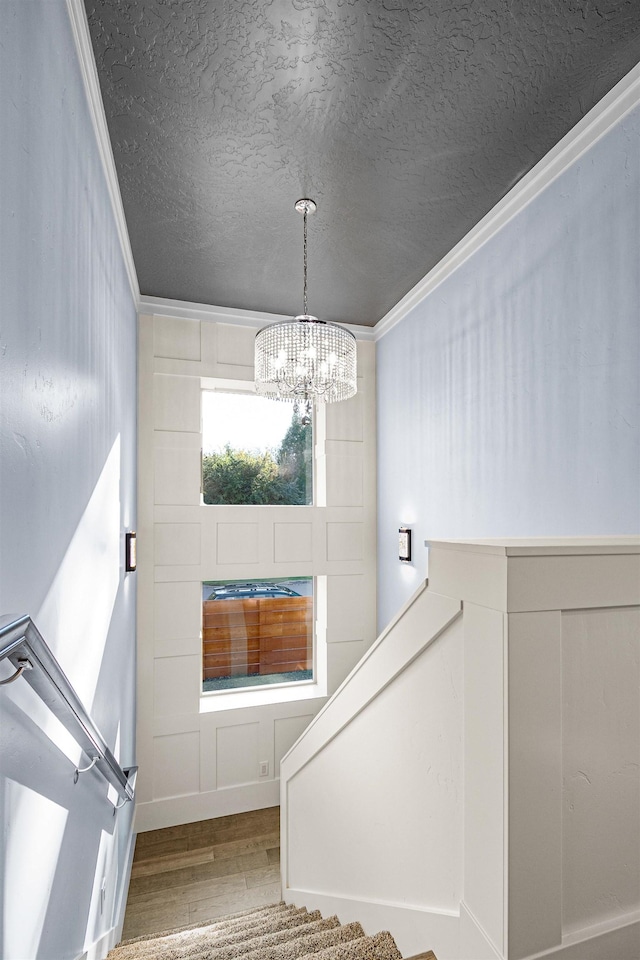 stairs with hardwood / wood-style flooring, a textured ceiling, crown molding, and a notable chandelier