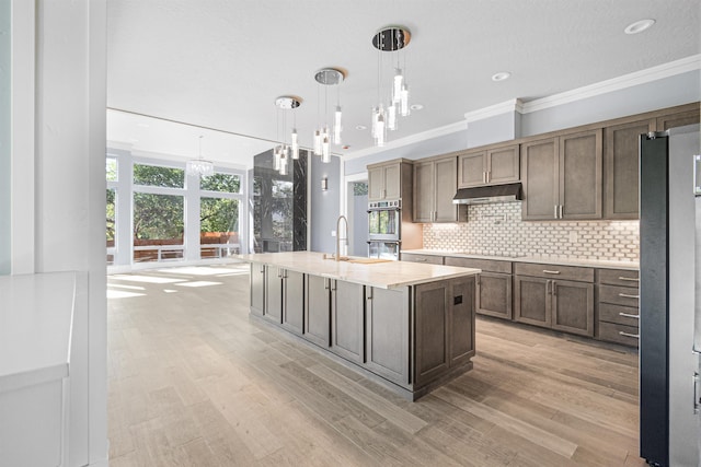 kitchen with pendant lighting, decorative backsplash, a kitchen island with sink, stainless steel appliances, and ornamental molding