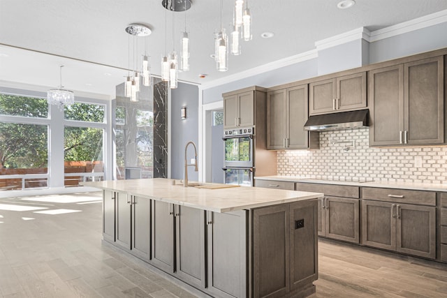 kitchen featuring sink, hanging light fixtures, a center island with sink, and stainless steel double oven