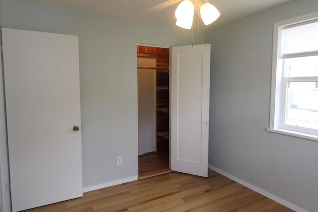 unfurnished bedroom featuring ceiling fan, a closet, a walk in closet, and light wood-type flooring