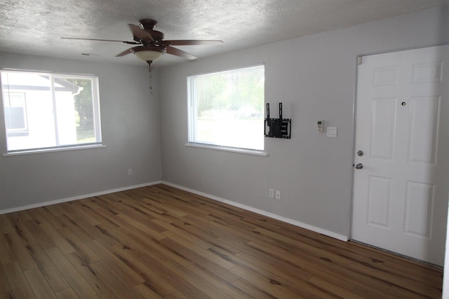 spare room featuring a healthy amount of sunlight, a textured ceiling, and dark hardwood / wood-style flooring