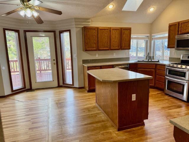 kitchen featuring vaulted ceiling with skylight, a kitchen island, sink, light hardwood / wood-style flooring, and appliances with stainless steel finishes