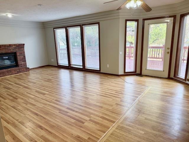 unfurnished living room with ceiling fan, plenty of natural light, light hardwood / wood-style flooring, and a brick fireplace