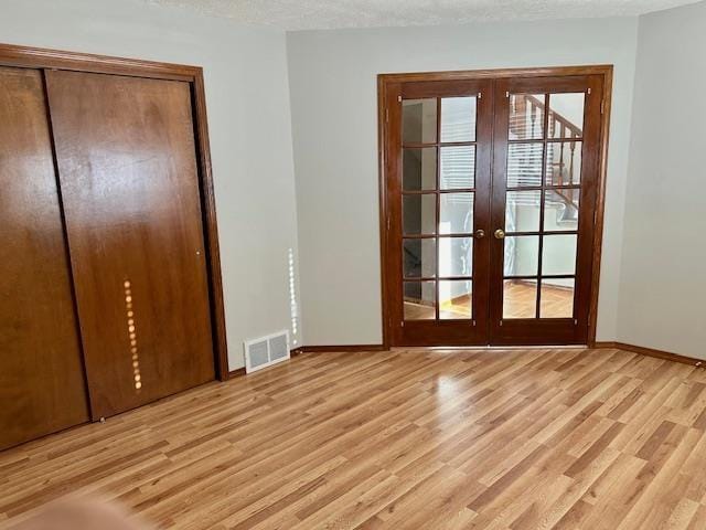 doorway with light wood-type flooring, a textured ceiling, and french doors