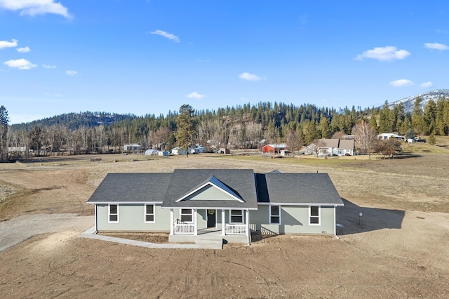 view of front of property featuring a porch, a forest view, and a shingled roof
