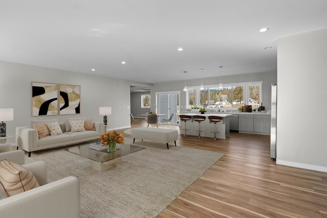 living room with recessed lighting, light wood-type flooring, a chandelier, and baseboards