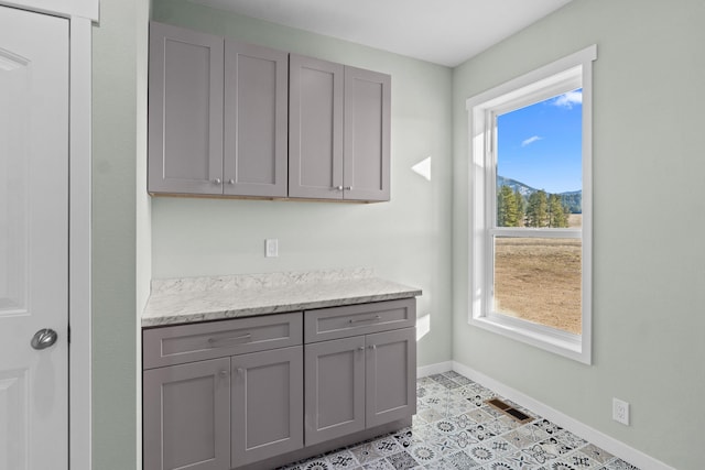 kitchen with light stone countertops, baseboards, and gray cabinetry