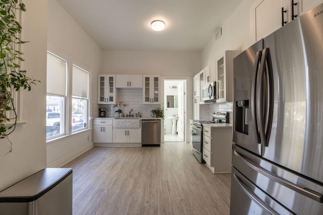 kitchen featuring sink, light hardwood / wood-style flooring, backsplash, stainless steel appliances, and white cabinets