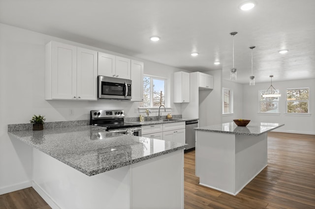 kitchen featuring kitchen peninsula, appliances with stainless steel finishes, dark wood-type flooring, pendant lighting, and white cabinets