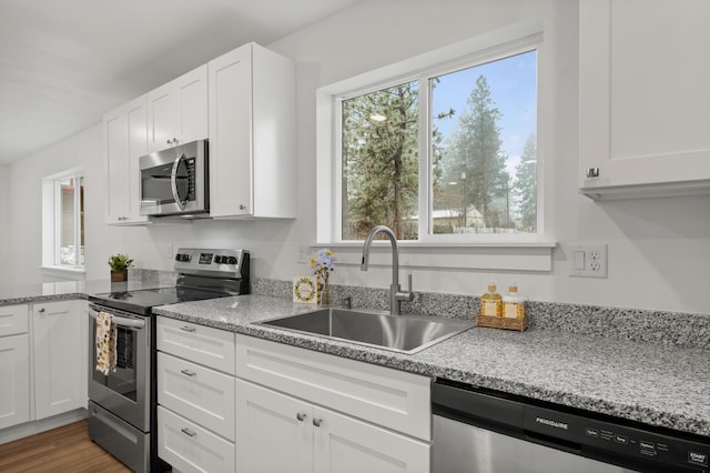 kitchen featuring appliances with stainless steel finishes, white cabinets, light stone counters, and sink