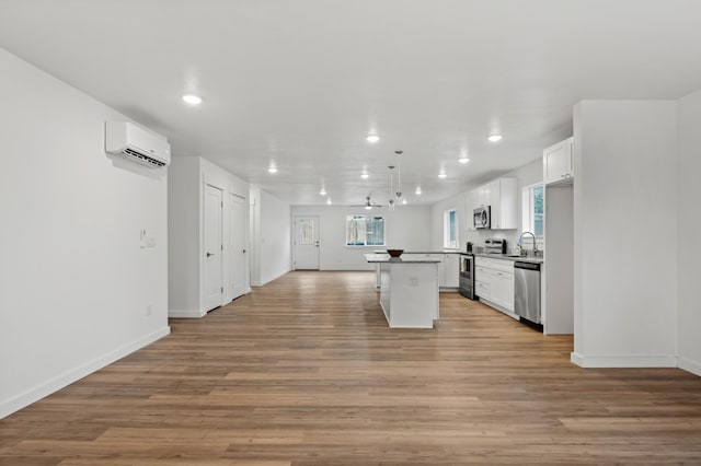 kitchen with an AC wall unit, appliances with stainless steel finishes, white cabinetry, and a center island