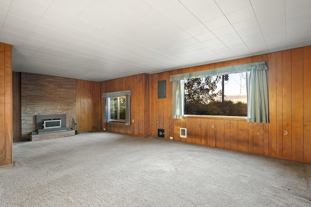 unfurnished living room featuring a brick fireplace, wood walls, electric panel, and carpet floors